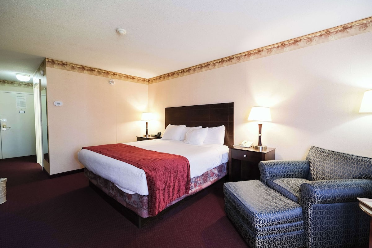 Quarto de hotel com uma cama grande, duas mesas de cabeceira com luminárias, uma cadeira e uma porta para o banheiro.