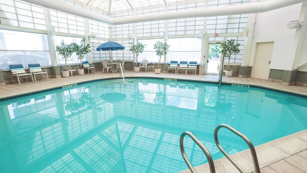 An indoor swimming pool with clear glass walls, lounge chairs, and potted plants. - Fireside Inn & Suites Portland (Portland)