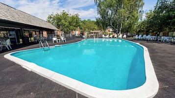 A swimming pool with a tiled deck, surrounded by lounge chairs and a covered seating area.