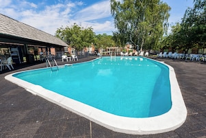 Una piscina con un borde empinado de baldosas, rodeada de sillas de descanso y una zona de estar techada.