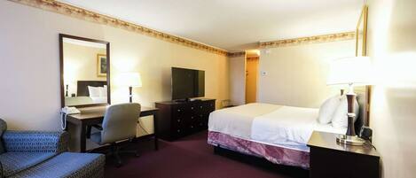 Habitación de hotel con cama, escritorio, silla, televisor, cómoda y espejo.