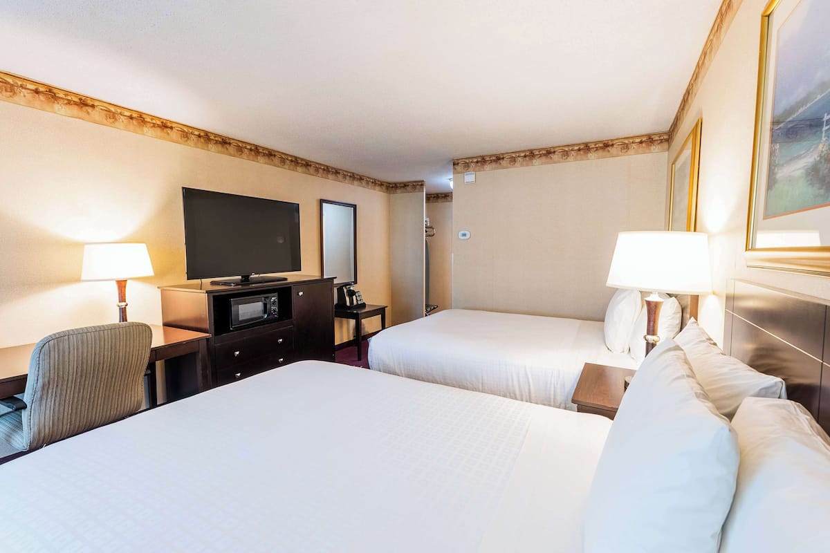 Quarto de hotel com duas camas, uma televisão, uma escrivaninha com abajur e uma cadeira.