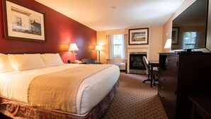 A hotel room with a large bed, a desk, a chair, a fireplace, and a television. - Fireside Inn & Suites Portland (Portland)