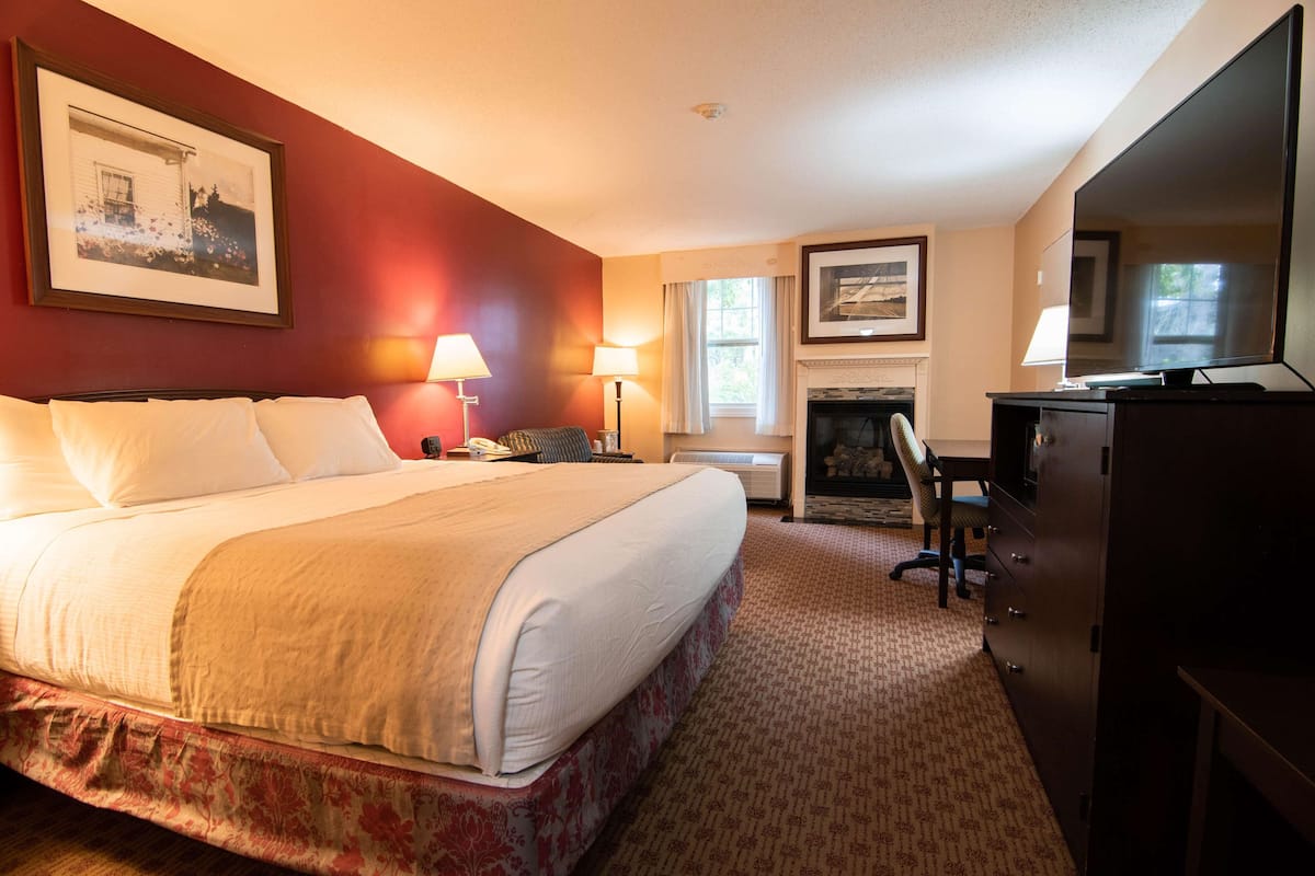Quarto de hotel com uma cama grande, uma escrivaninha, uma cadeira, lareira e televisão.
