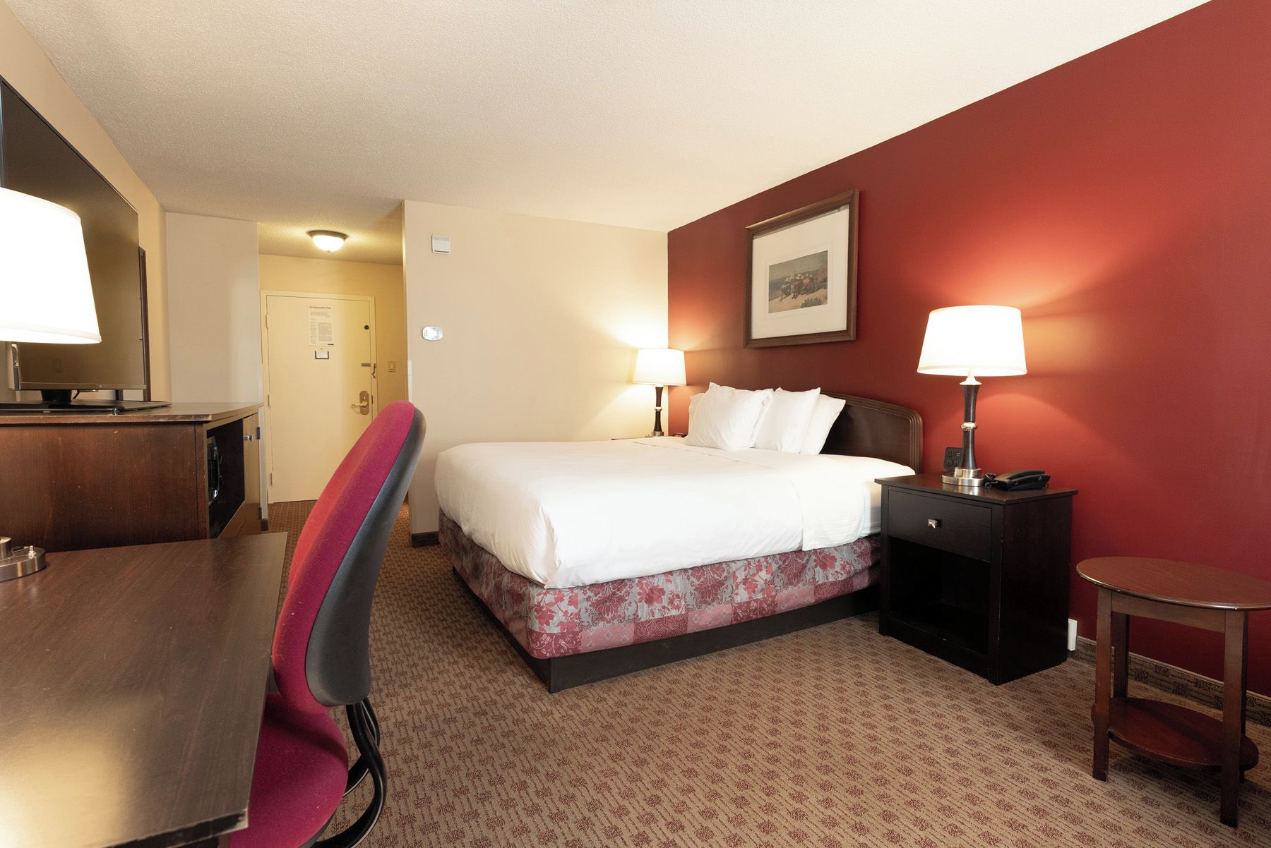 A hotel room with a bed, bedside tables, a desk, and a chair.