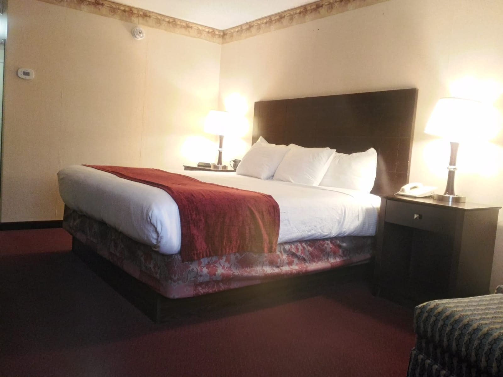 Une chambre d’hôtel avec un lit, des lampes de chevet, une table de chevet et une moquette rouge.