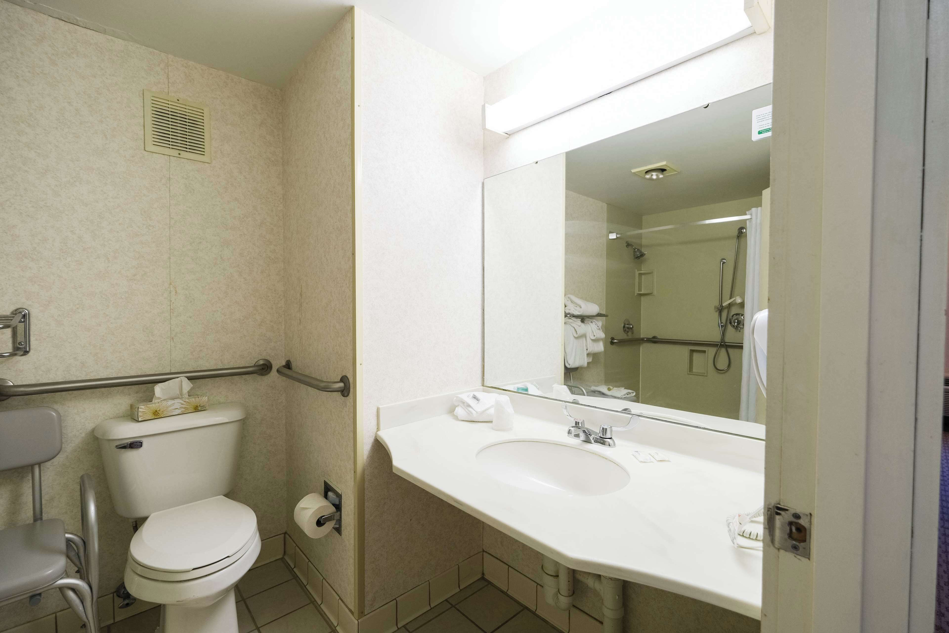 A bathroom with a toilet, sink, mirror, and shower.