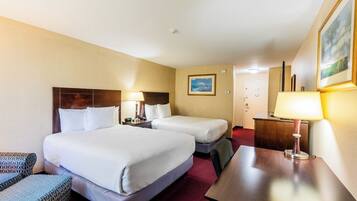 A hotel room with two beds, a desk, a chair, and a lamp.