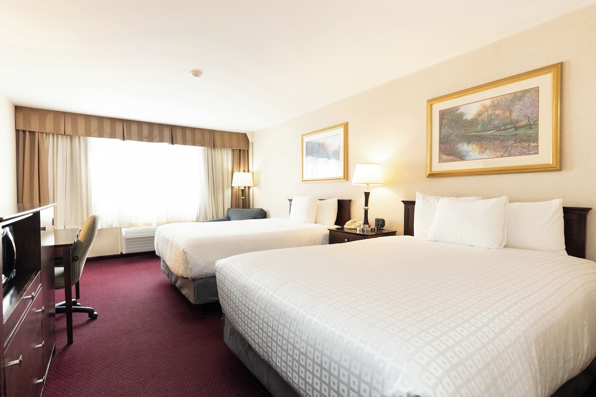 A hotel room with two beds, a desk, a chair, and a painting on the wall.