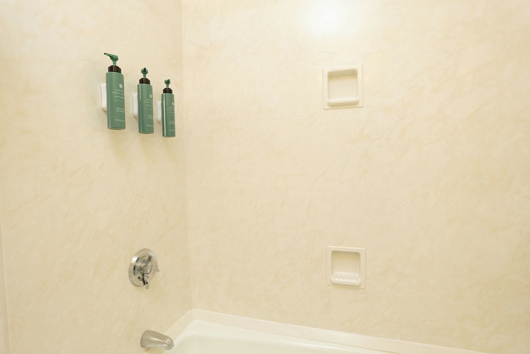 A bathroom with a bathtub, a showerhead, and three green bottles on the wall.