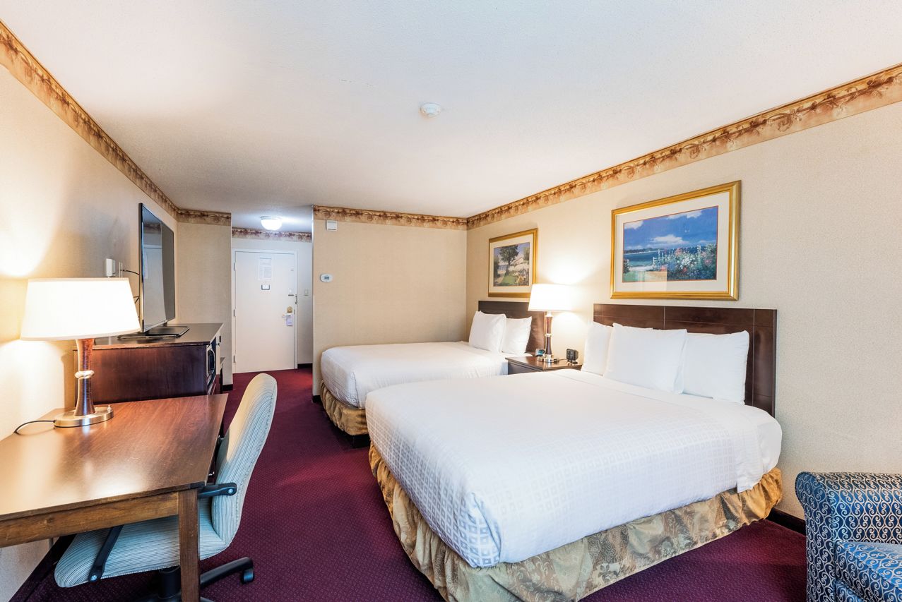 A hotel room with two beds, a desk with a chair, a lamp, and a framed picture on the wall.