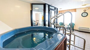 A hot tub with a metal ladder, a clock on the wall, and a view of the room with chairs and a table. - Fireside Inn & Suites Portland (Portland)