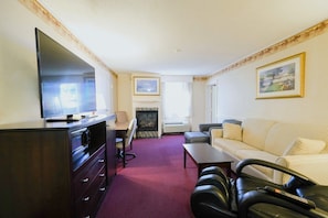 A hotel room with a television, a fireplace, a sofa, a desk, and a chair. - Fireside Inn & Suites Portland (Portland)