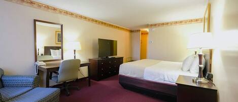 Ein Hotelzimmer mit Bett, Schreibtisch, Stuhl, Fernseher, Kommode und Lampen.