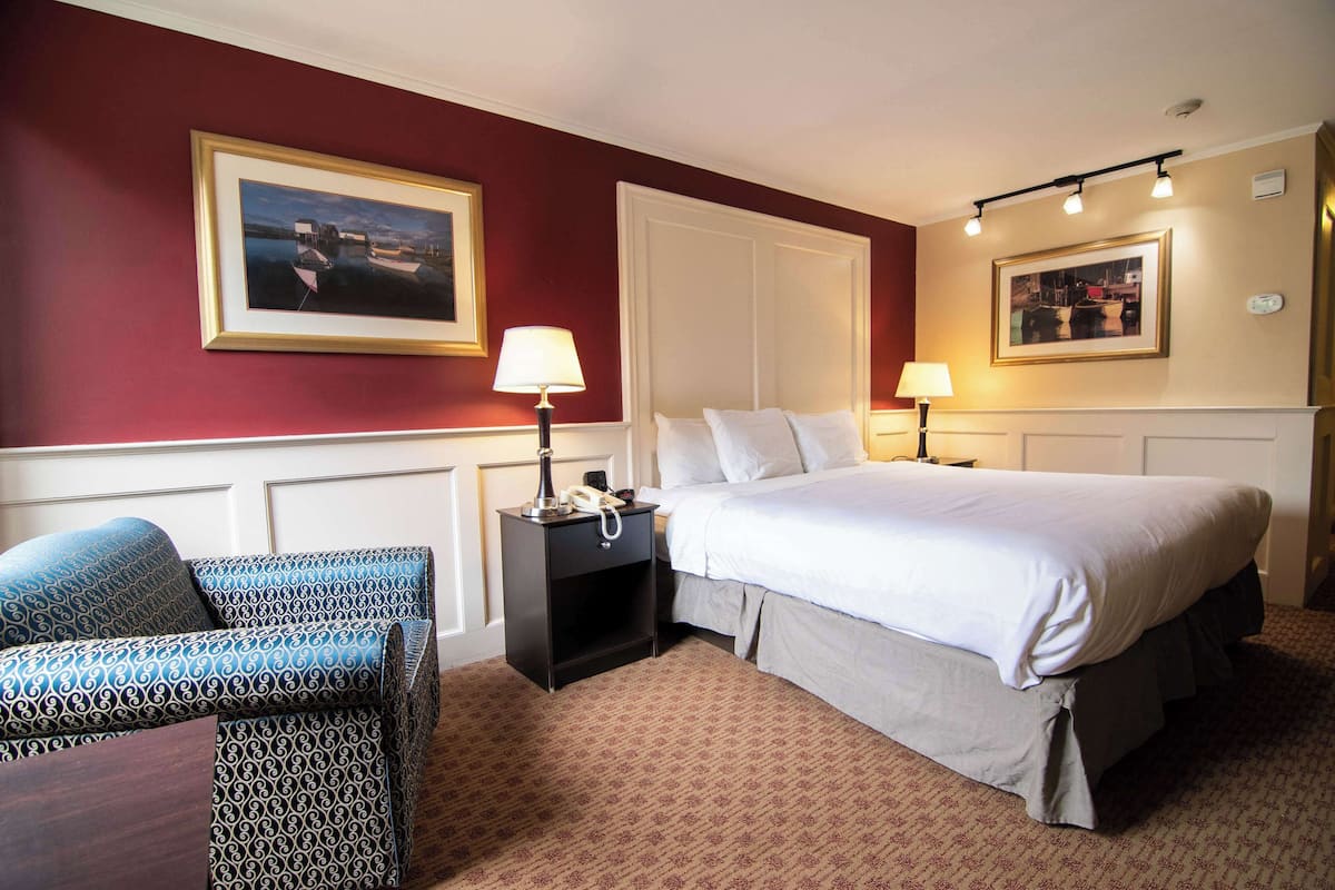 Quarto de hotel com uma cama grande, duas mesas de cabeceira com luminárias, uma cadeira e duas imagens emolduradas nas paredes.