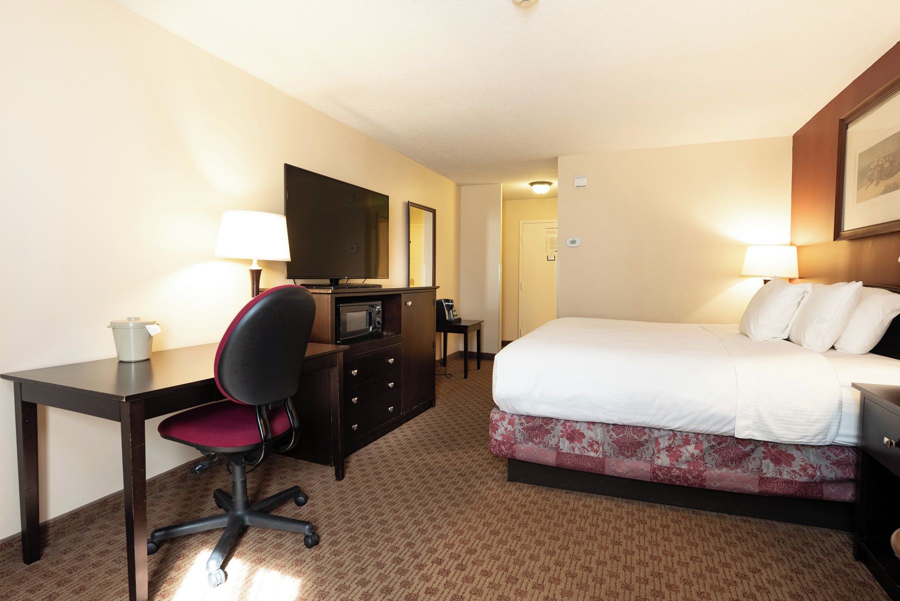 A hotel room with a bed, desk, chair, television, and a microwave.