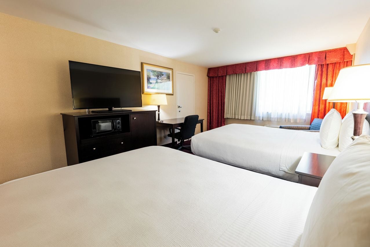 Una habitación de hotel con dos camas, televisor, escritorio y lámpara.