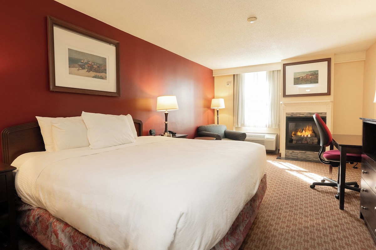 A hotel room with a large bed, a fireplace, a desk, and a chair.