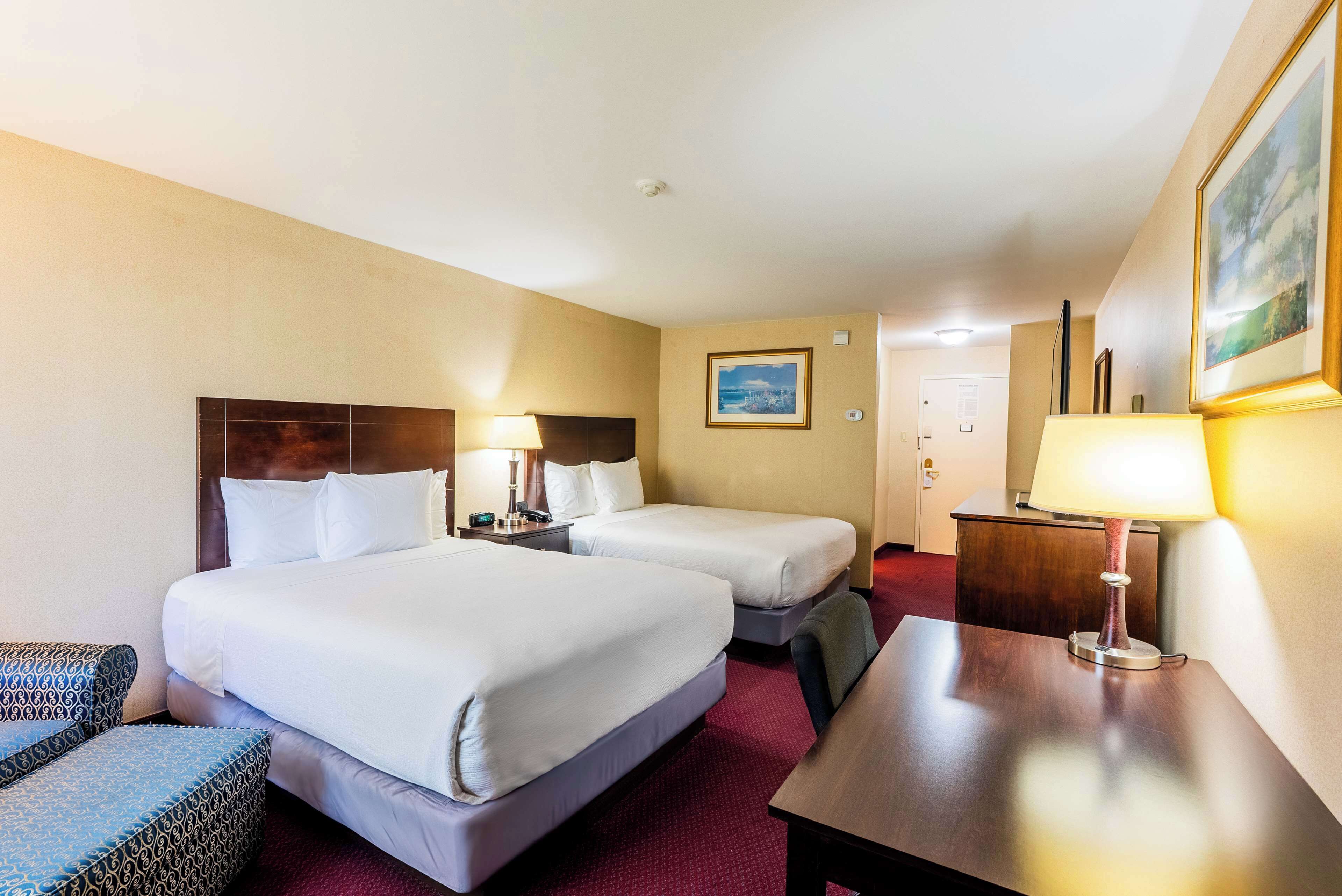 A hotel room with two beds, a desk, a chair, and a lamp.