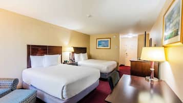 A hotel room with two beds, a desk, a chair, and a lamp.