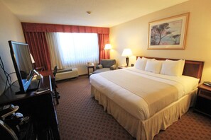 A hotel room with a large bed, a desk with a computer, a chair, a lamp, and a painting on the wall.