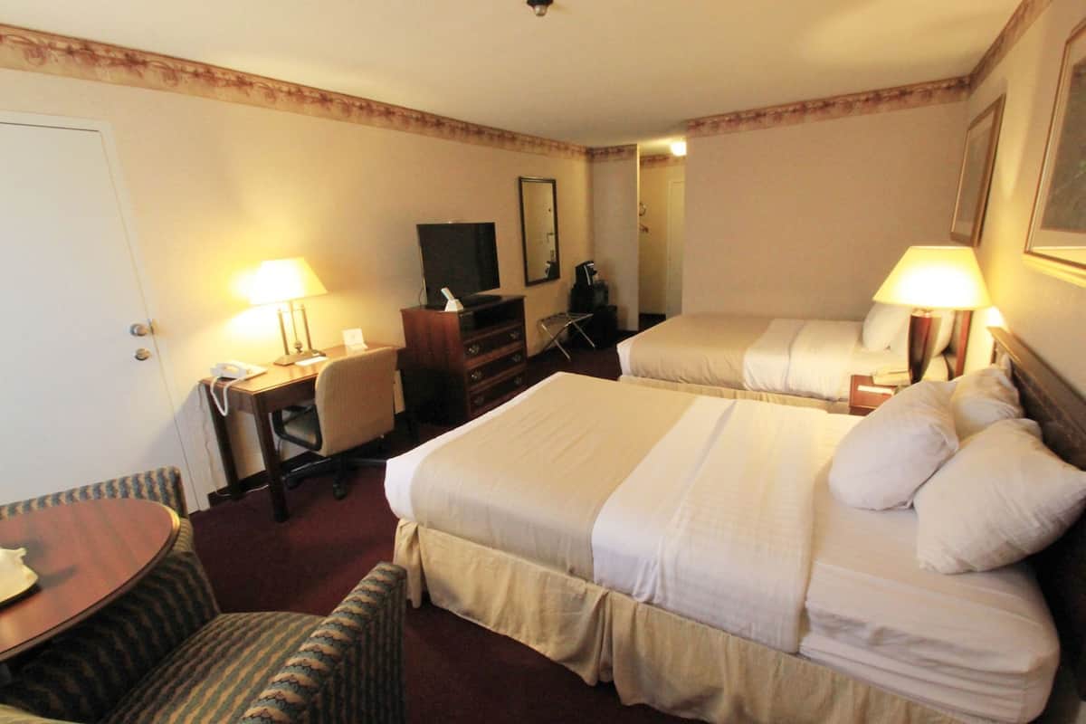 Quarto de hotel com duas camas, uma escrivaninha com cadeira, telefone, televisão e duas luminárias.
