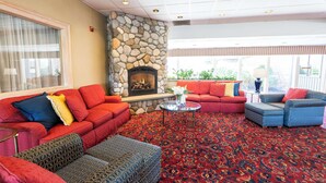 A spacious lobby with a stone fireplace, red and blue upholstered seating, and a patterned carpet. - Fireside Inn & Suites Portland (Portland)