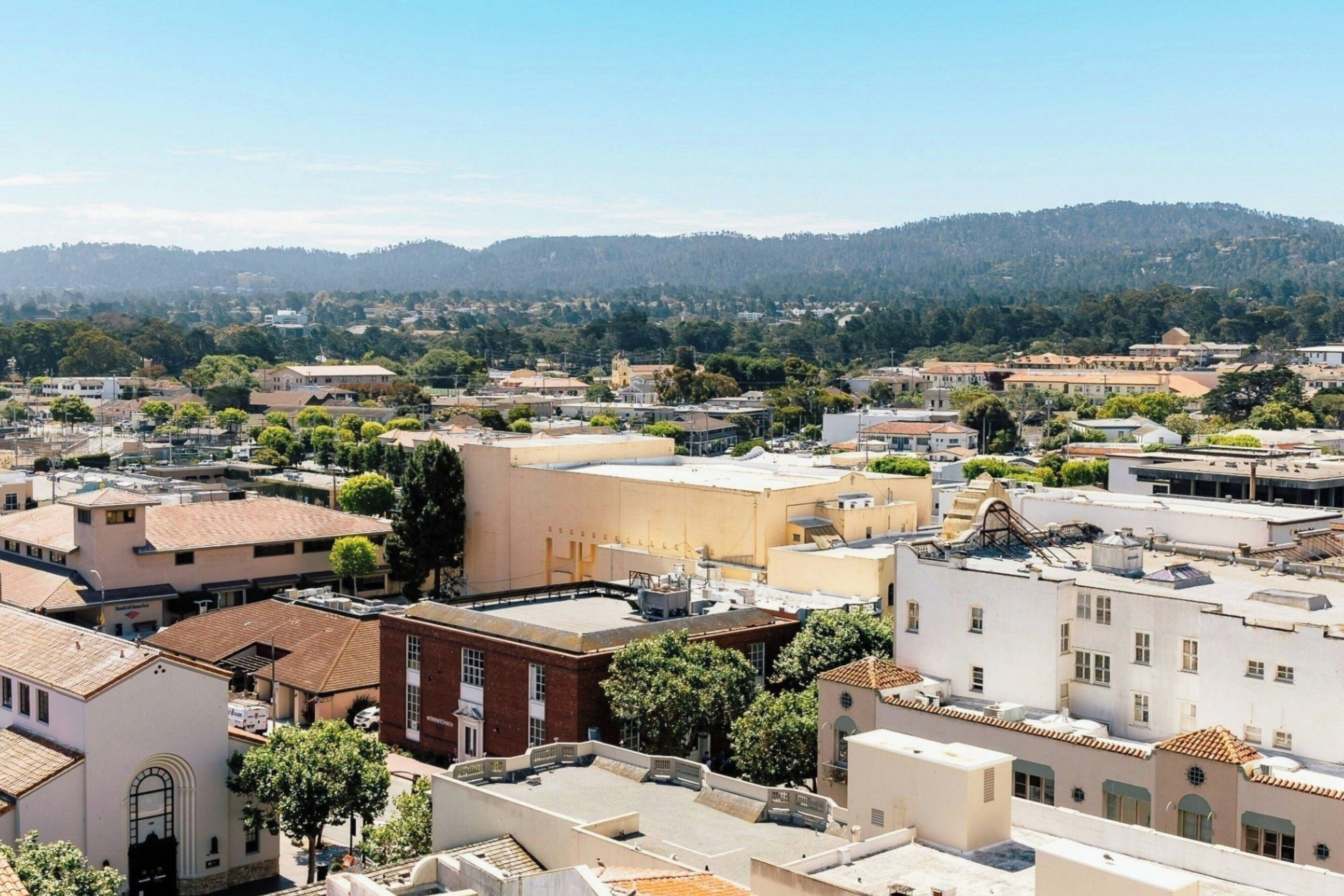 Un paisaje urbano con una combinación de edificios residenciales y comerciales, un banco destacado y un telón de fondo montañoso.