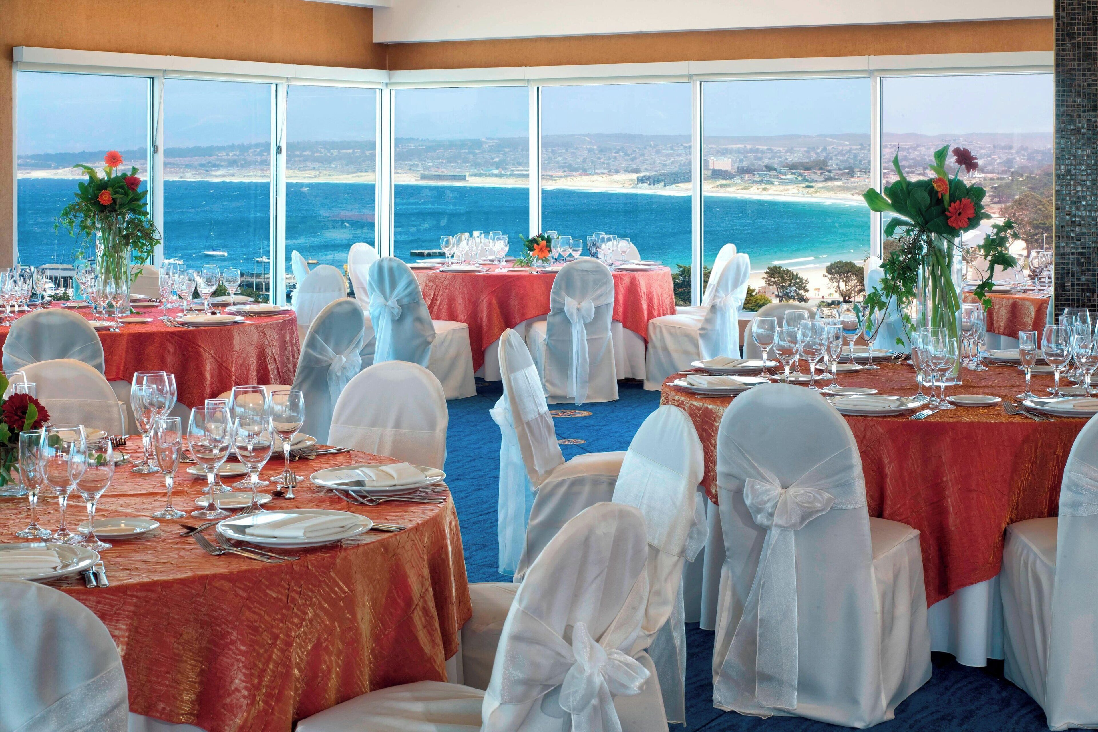 A banquet hall with tables set for a formal event, overlooking a coastal view.