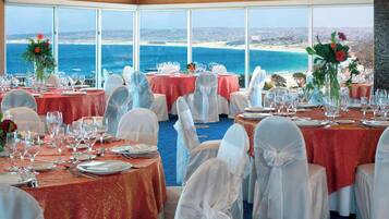 A banquet hall with tables set for a formal event, overlooking a coastal view.
