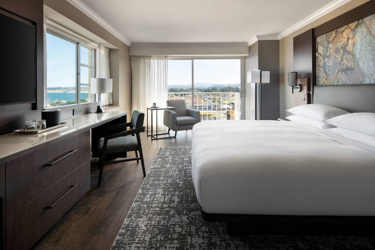 Habitación de hotel moderna con una cama grande, un escritorio con silla, televisor de pantalla plana y un ventanal con vista a la ciudad.