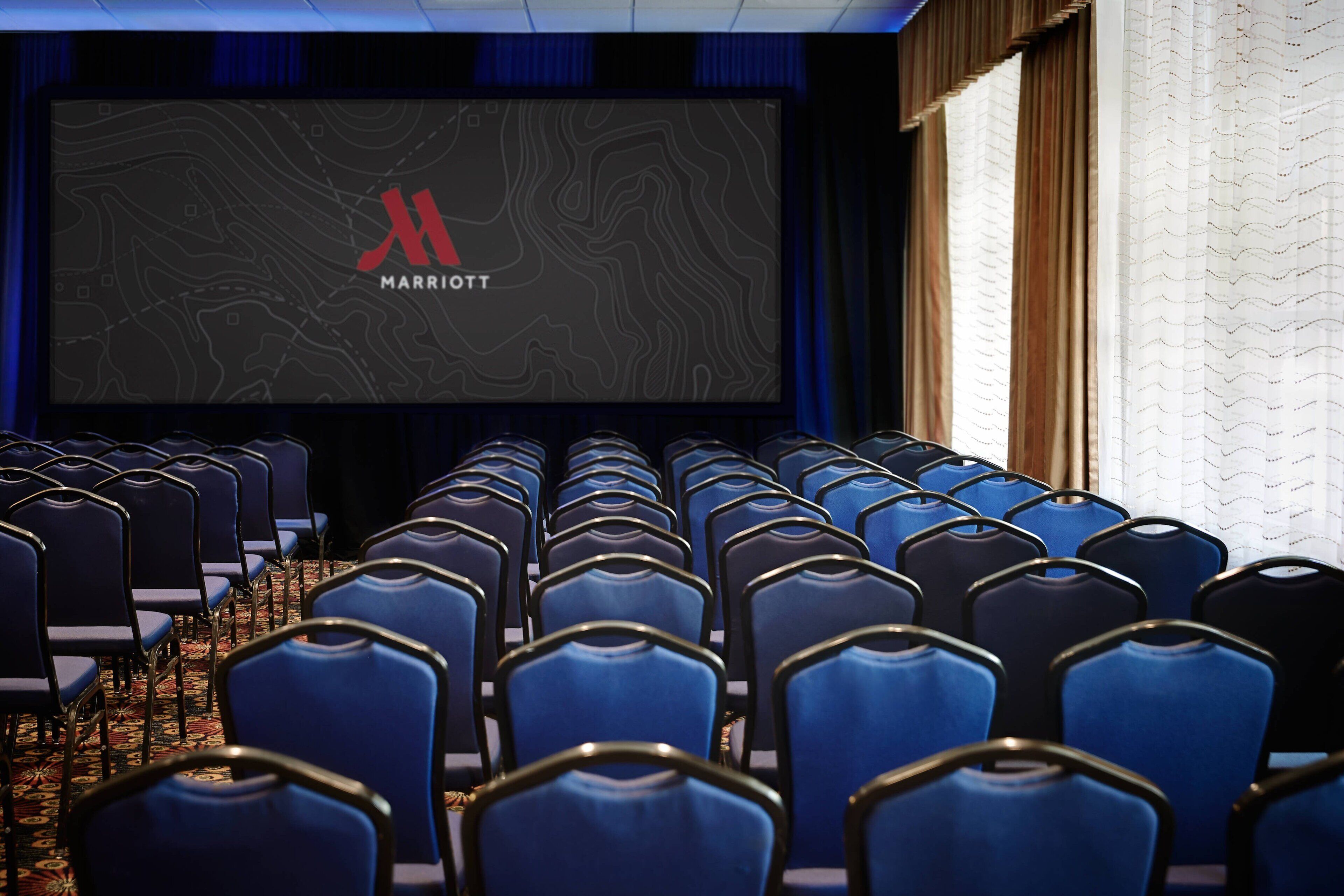 Une salle de théâtre avec des rangées de sièges bleus et un grand écran affichant le logo de Marriott.