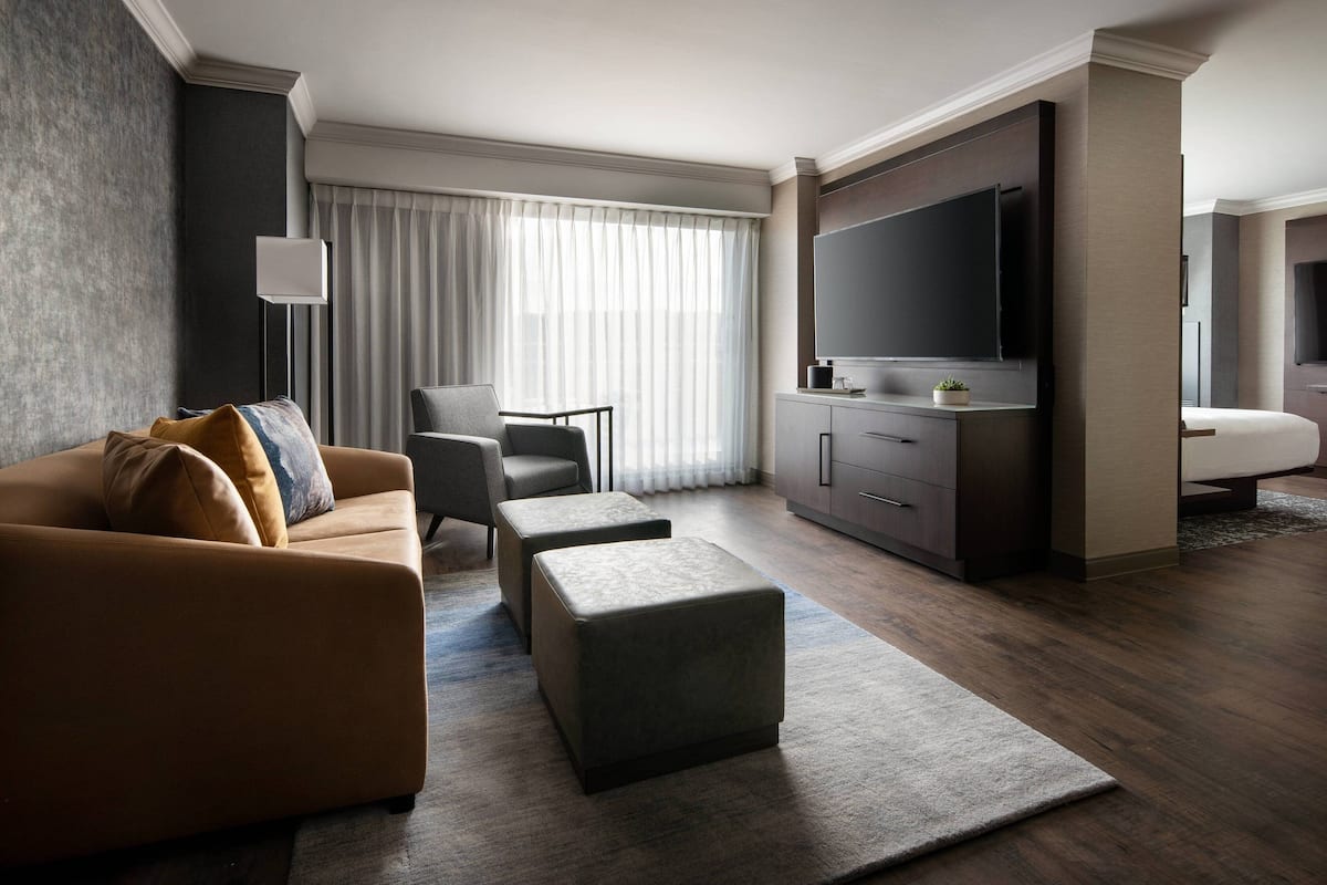 Una habitación de hotel moderna con sofá, reposapiés, televisor de pantalla plana y escritorio con lámpara.