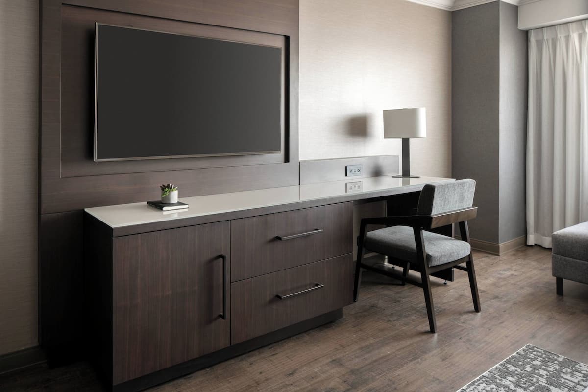 Una habitación de hotel moderna con un televisor de pantalla plana grande montado en la pared, un escritorio con una lámpara y una silla cómoda.