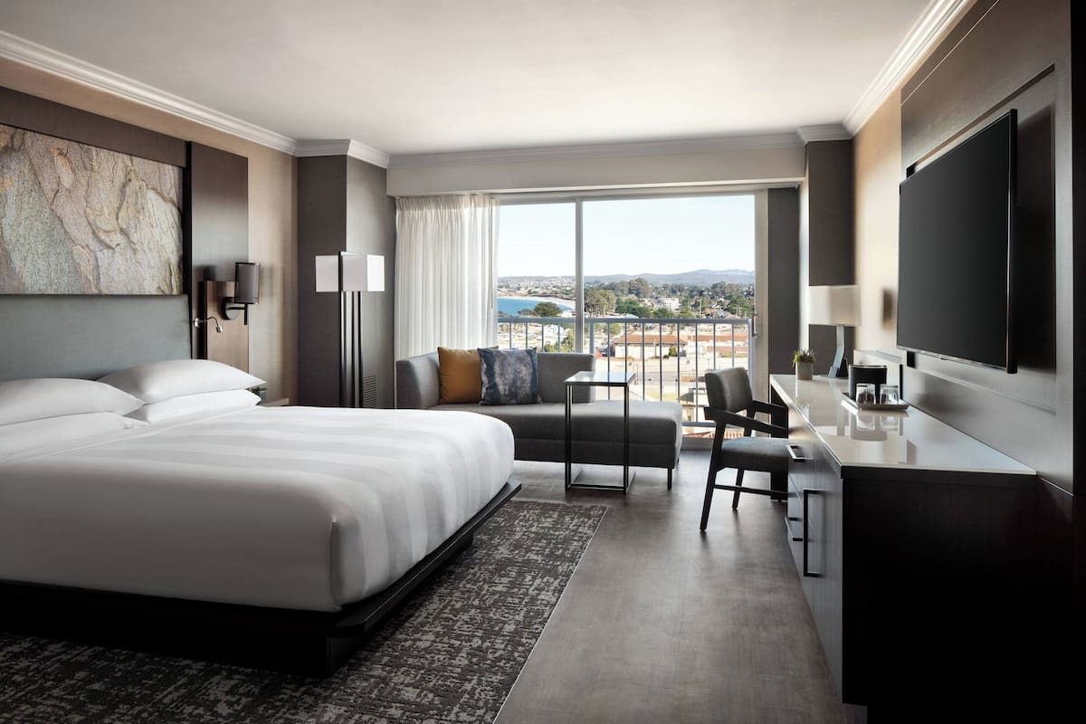 Una habitación de hotel moderna con una cama grande, un escritorio, una silla y vistas a la ciudad.