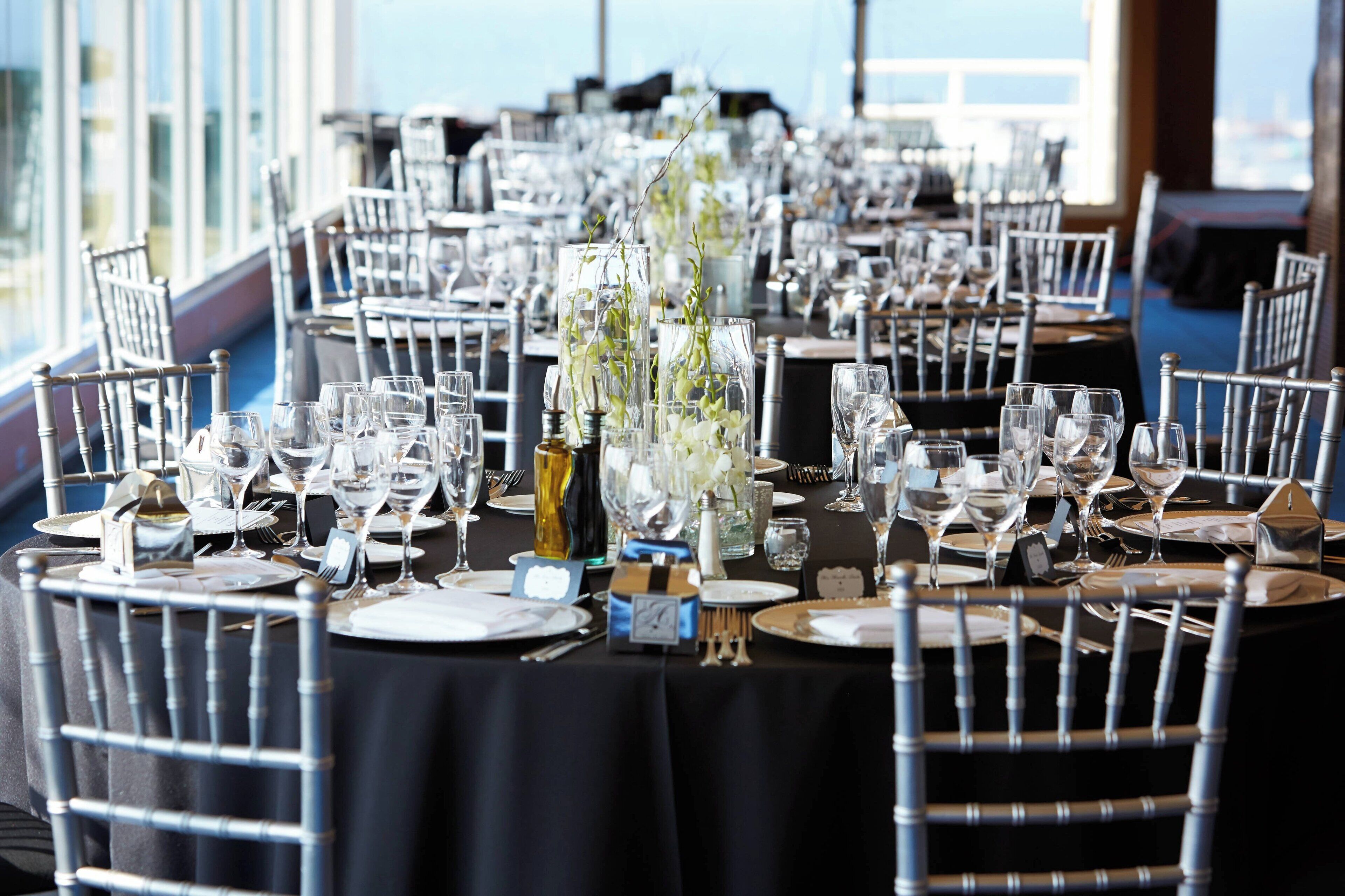 Une salle de banquet avec des tables rondes dressées pour un événement formel, agrémentée de verres, d’assiettes et de couverts en argent.