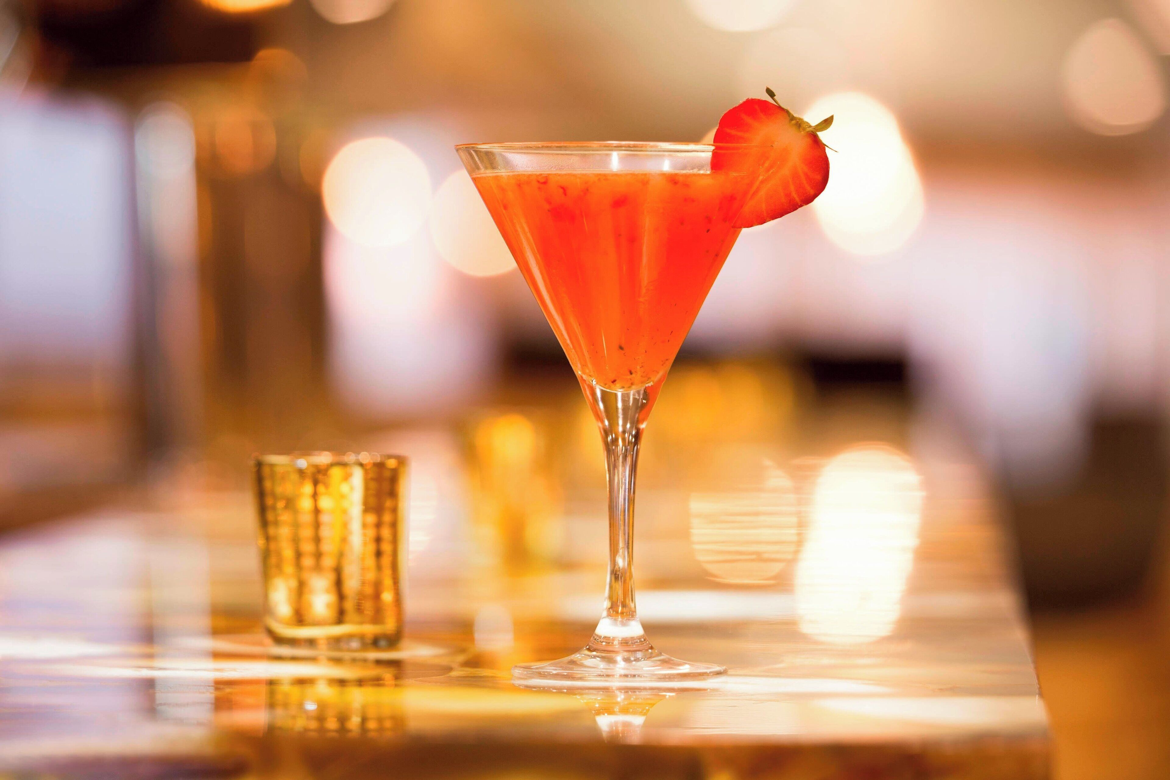 Un cocktail servi dans un verre à martini, garni d’une fraise, posé sur le comptoir d’un bar.