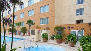 A hotel pool area with a hot tub, surrounded by potted plants and a building with multiple windows.