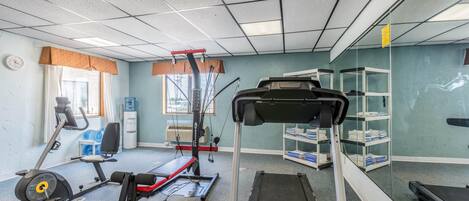 Une salle de sport équipée de machines de cardio, de bancs de musculation et dotée d’un mur recouvert de miroirs.