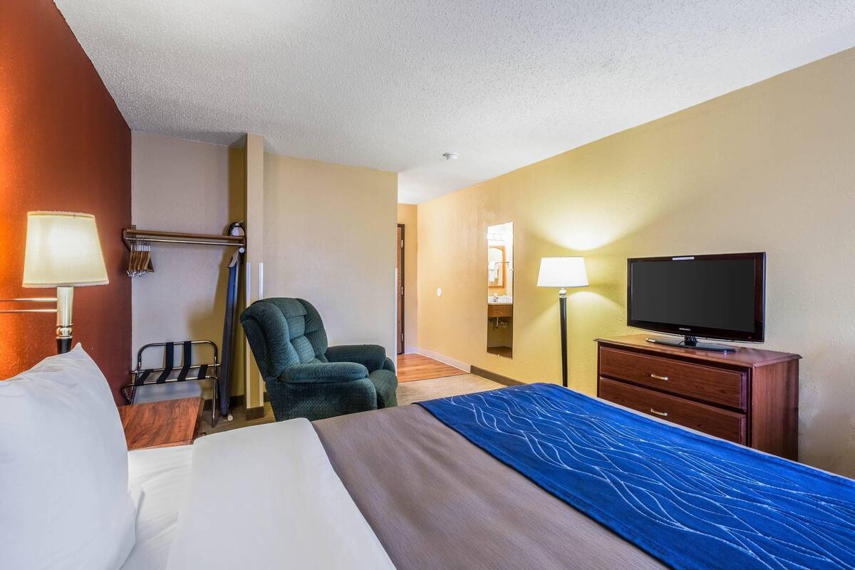 Ein Hotelzimmer mit einem Bett, einem Fernseher, einem Sessel, einem Schreibtisch und einer Lampe.