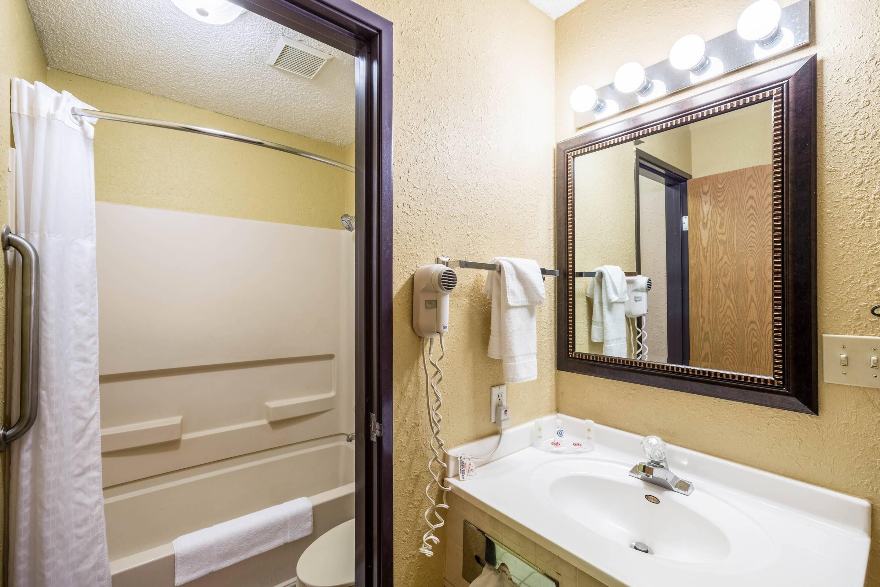 Un baño con ducha, inodoro, lavabo y un espejo con iluminación.