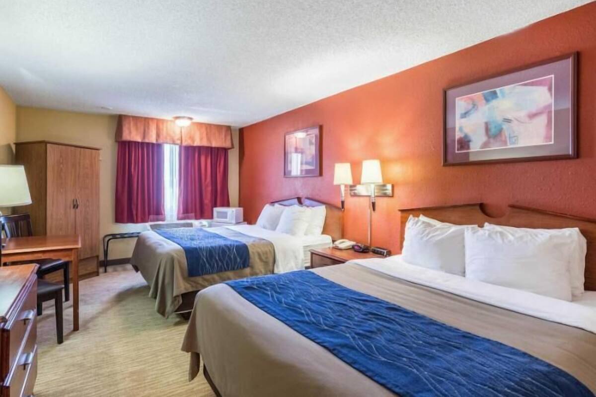 Ein Hotelzimmer mit zwei Betten, einem Schreibtisch, einem Stuhl, einem Kleiderschrank und einem Bild an der Wand.
