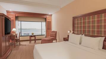 A hotel room with a large bed, a desk with a chair, a television, and a window with a view of the sea.