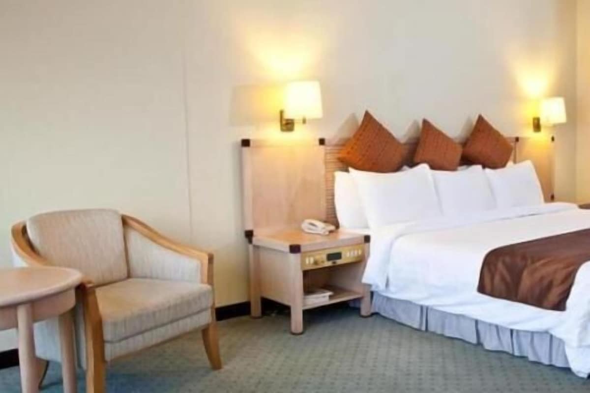 Una habitación de hotel con cama, mesita de noche, silla y lámparas.