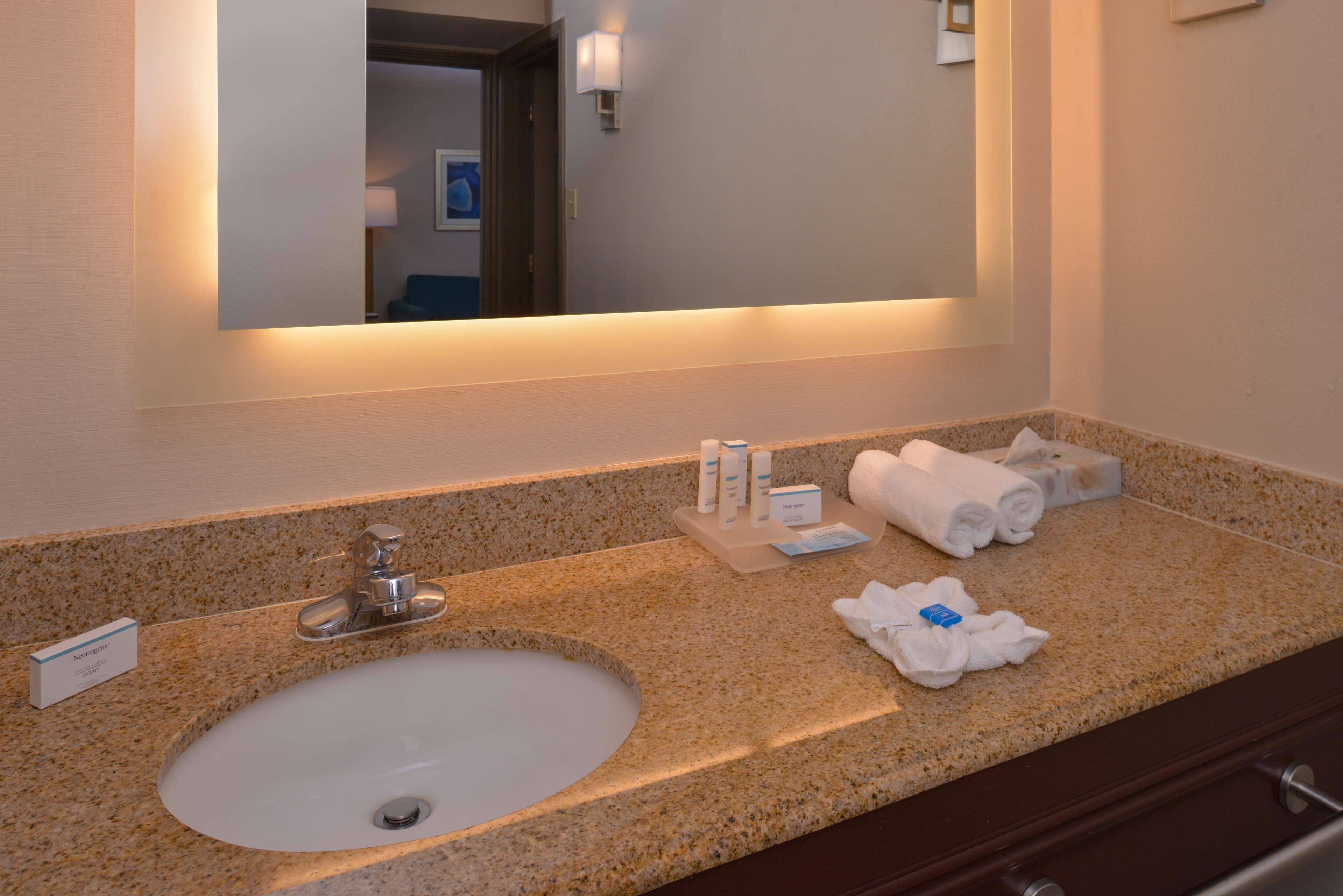 A hotel bathroom with a granite countertop sink, a mirror, and toiletries.