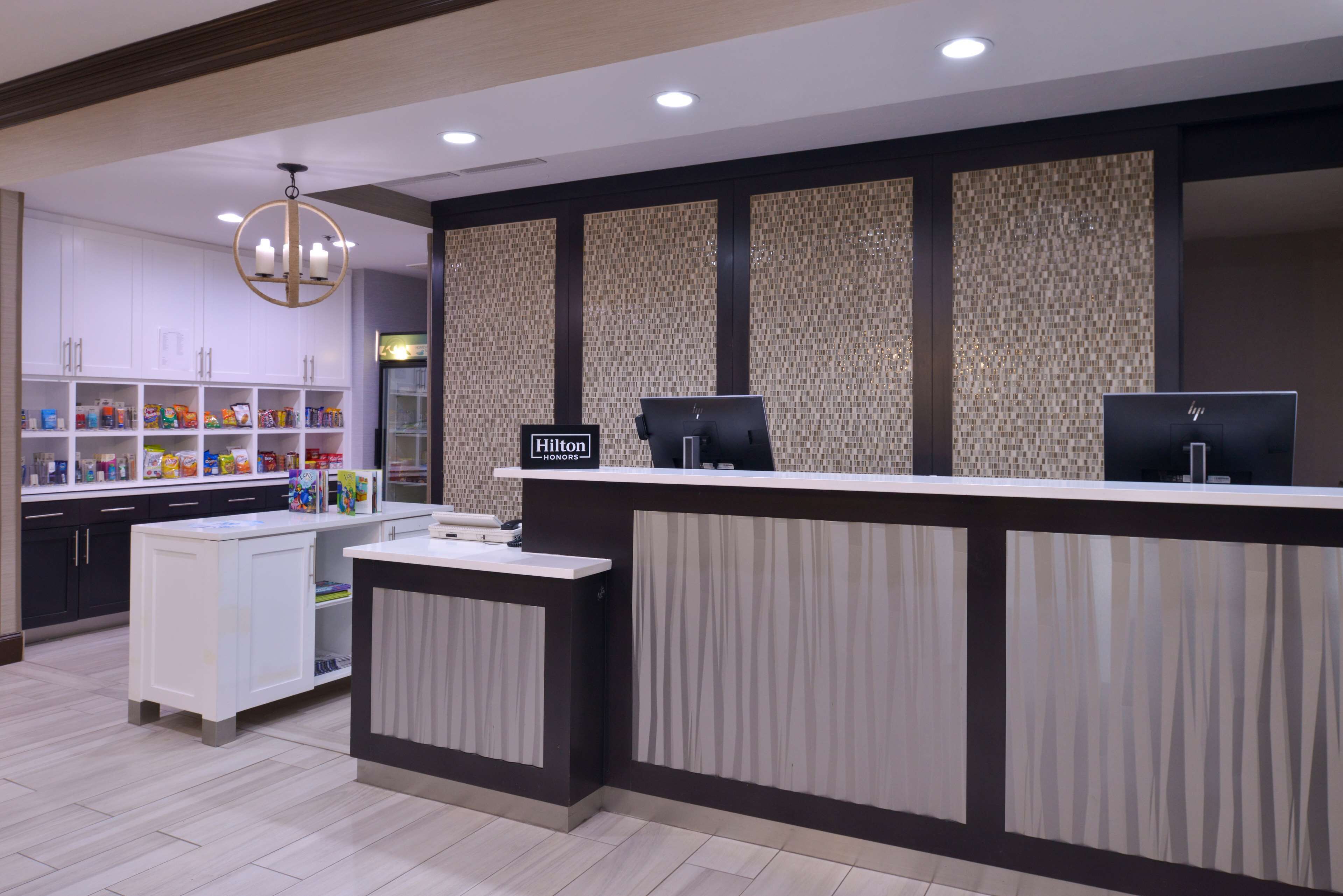 Un espace d’accueil d’hôtel au design moderne, comprenant un comptoir de réception, un minibar et divers équipements disposés sur des étagères.