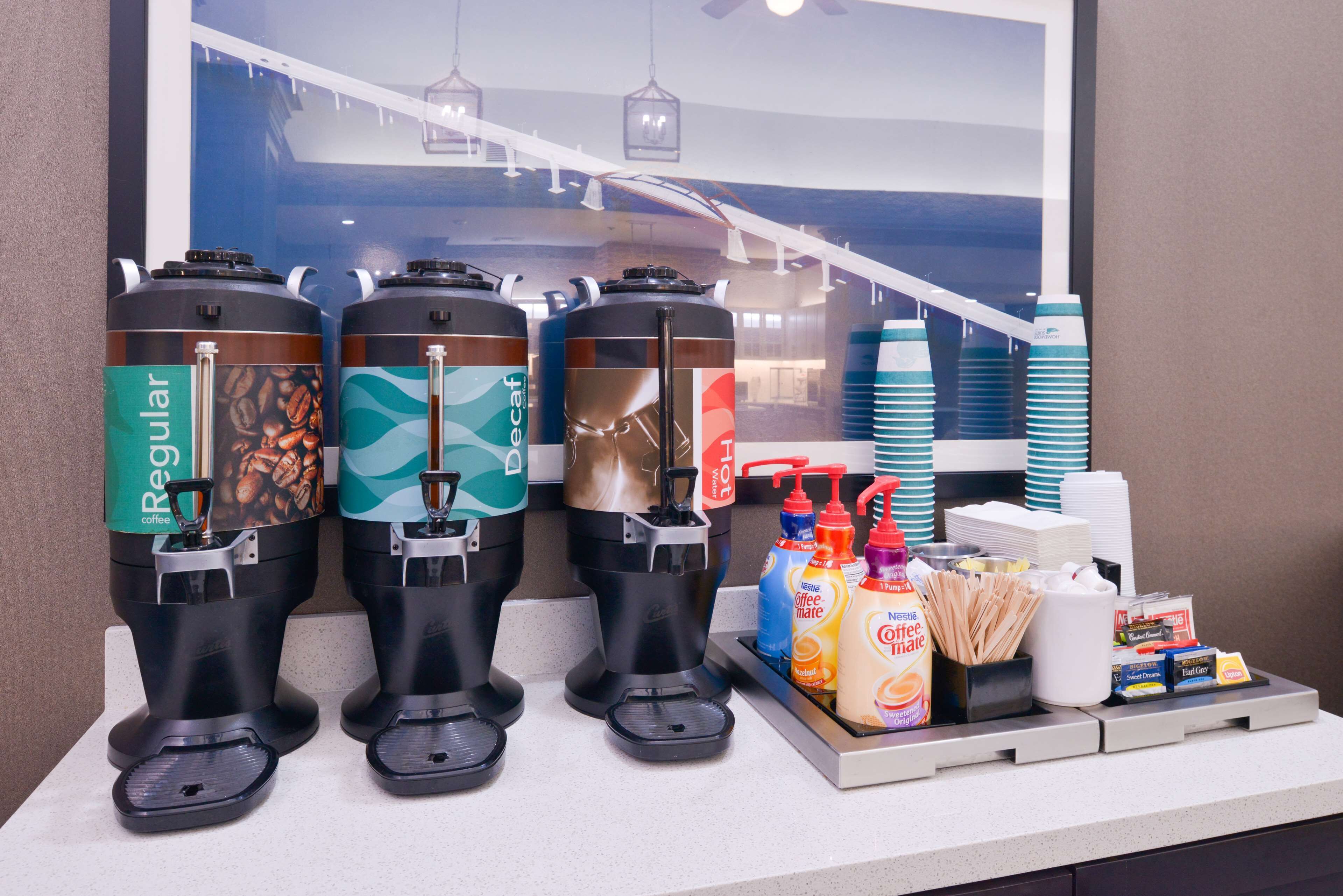A coffee station with three dispensers labeled 'Regular,' 'Decaf,' and 'Hot,' and a tray with coffee creamer, sugar packets, and napkins.