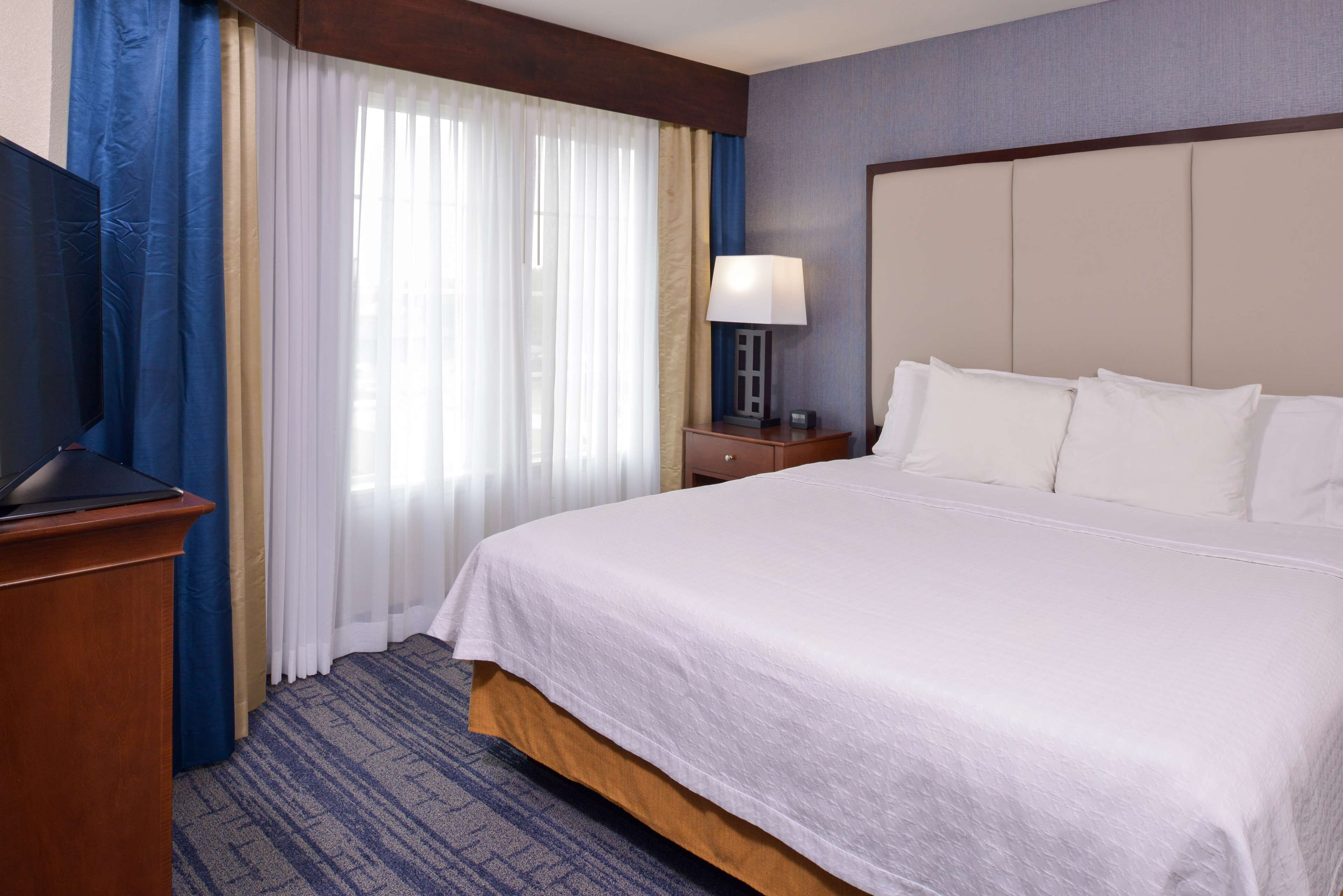 A hotel room with a large bed, a desk with a lamp, and a television.