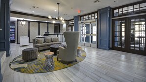 Un vestíbulo amplio con un sofá, sillones y una mesita de centro. Un tapete con diseño cubre el suelo, y las paredes están decoradas con cuadros enmarcados.