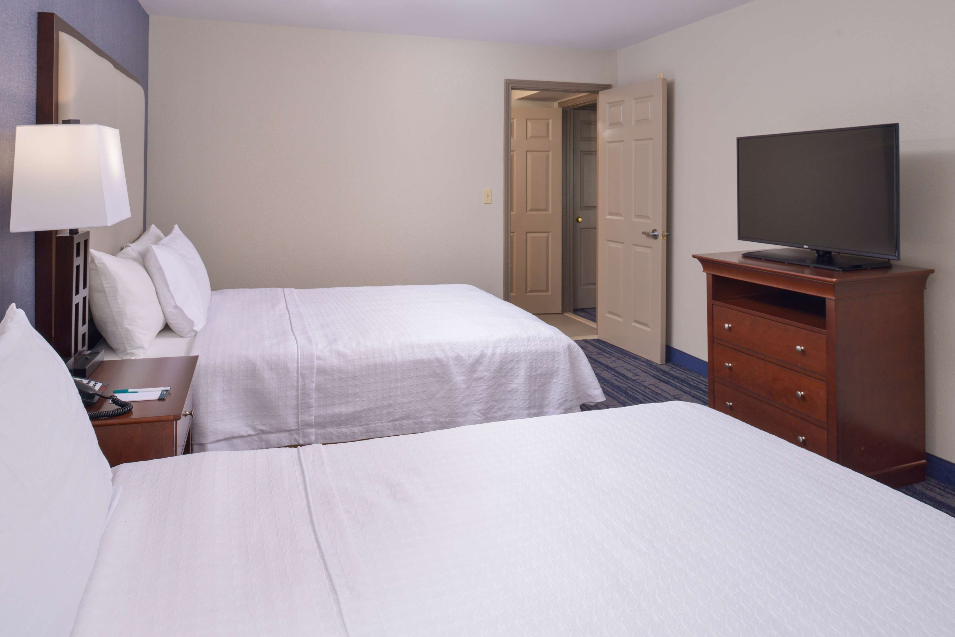 A hotel room with two beds, a television on a wooden stand, a desk with a lamp, and a door leading to another room.